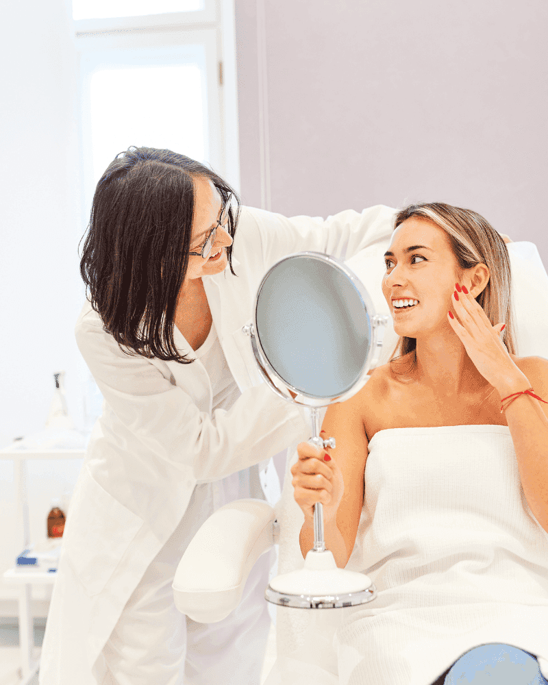 Doctor examining a smiling woman's face with a mirror in a clinic.