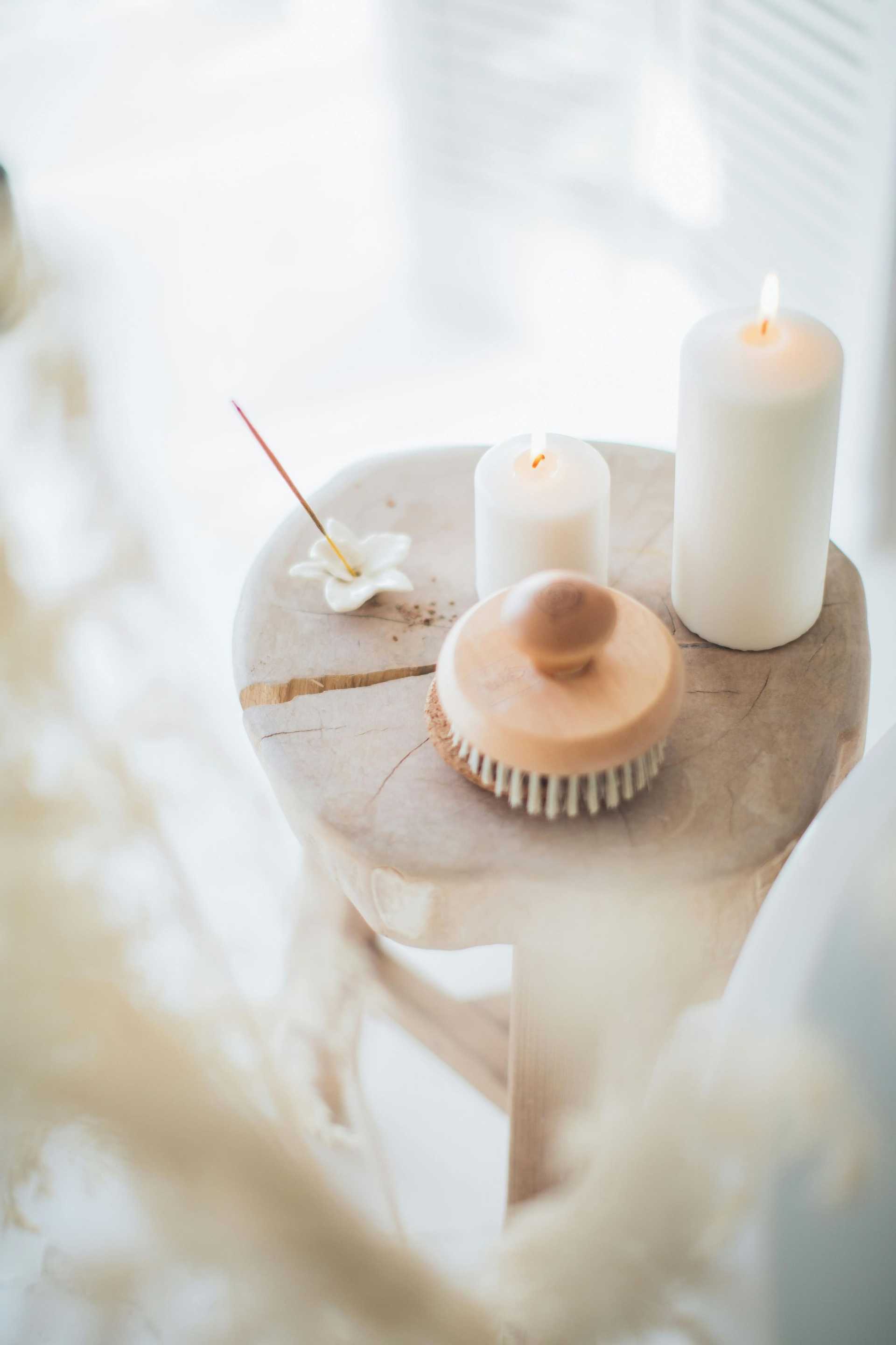 A wooden stool with candles, incense, a brush, and a ceramic flower creating a serene atmosphere.
