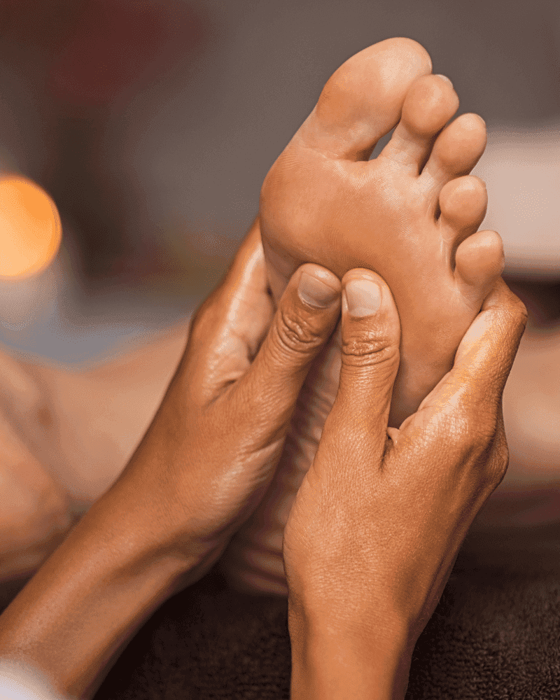 Close-up of hands giving a relaxing foot massage in a tranquil spa setting with dim lighting.
