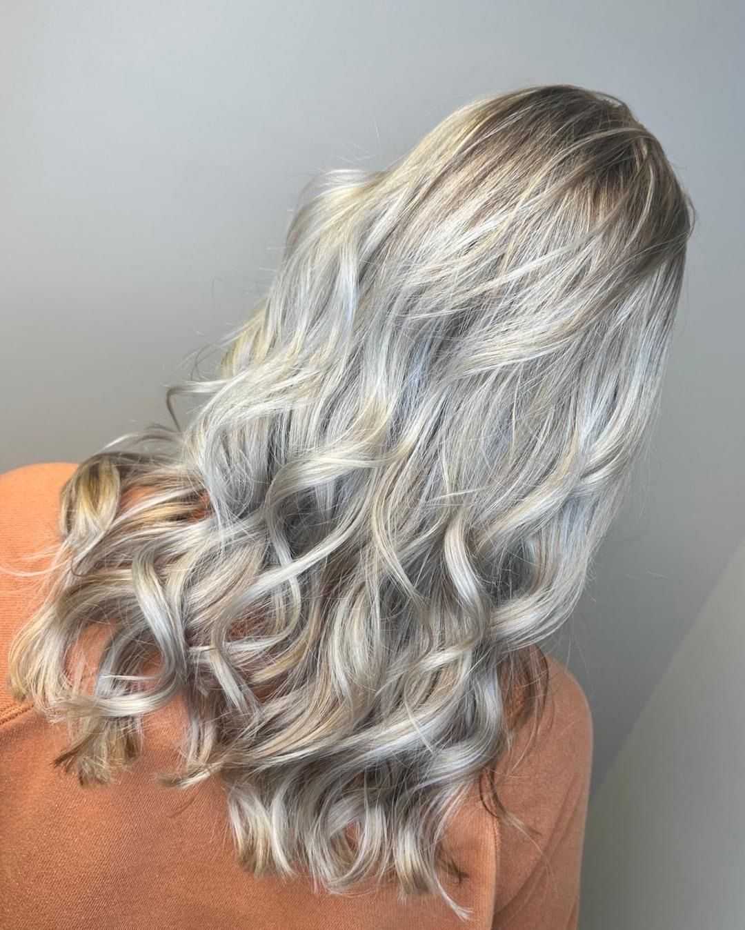 Woman with long, wavy, silver-blonde hair wearing an orange top, facing away.