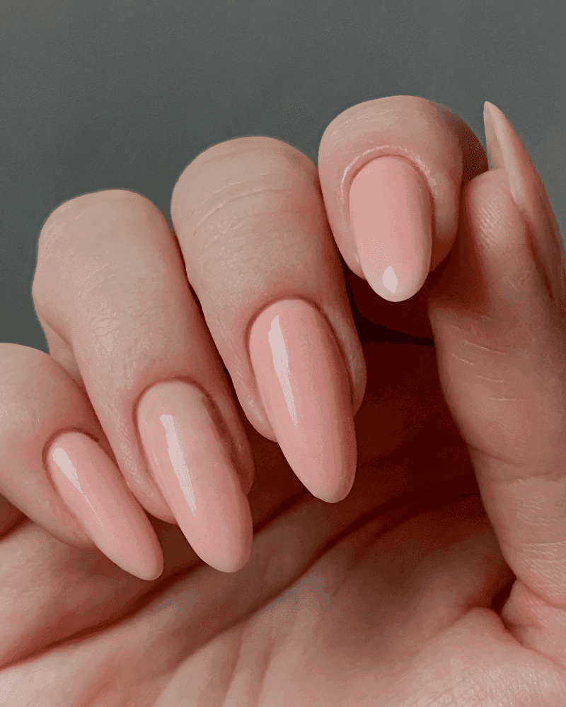 A hand displaying neatly manicured, glossy pink nails against a gray background.