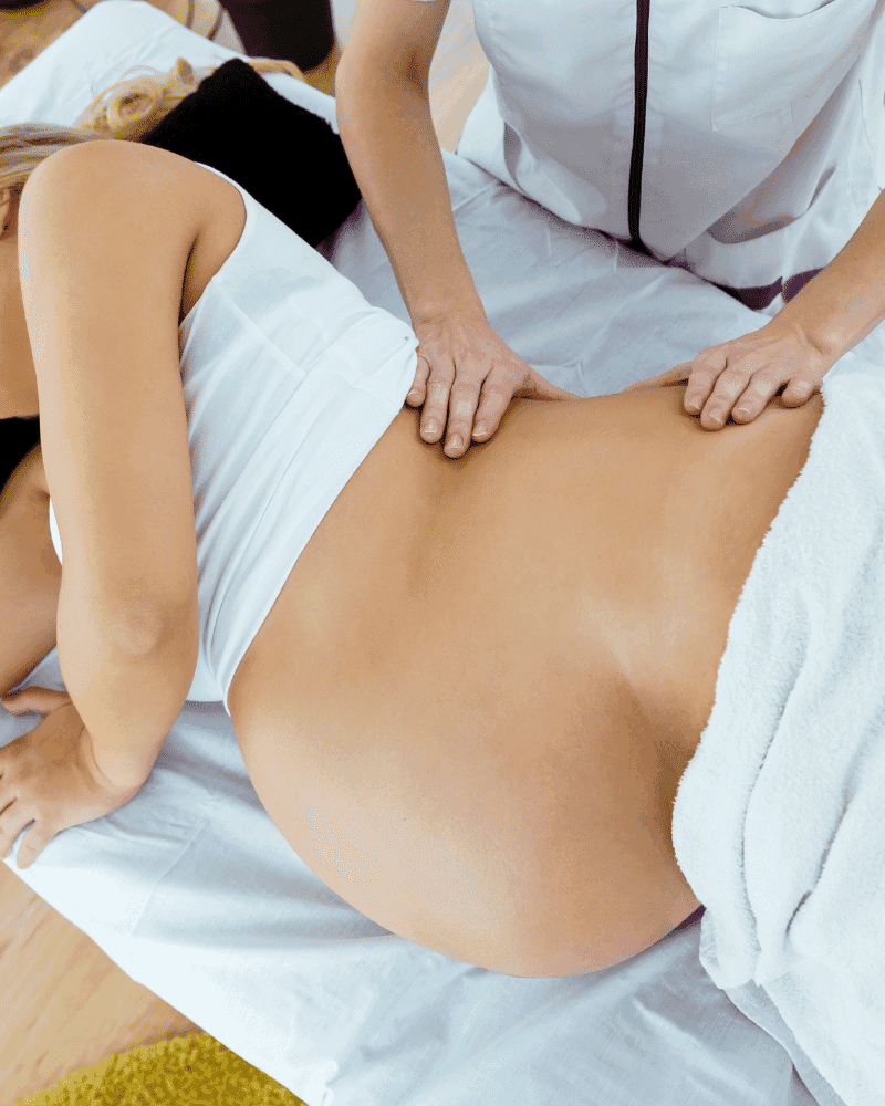 Pregnant woman receiving a back massage from a therapist in a serene setting.