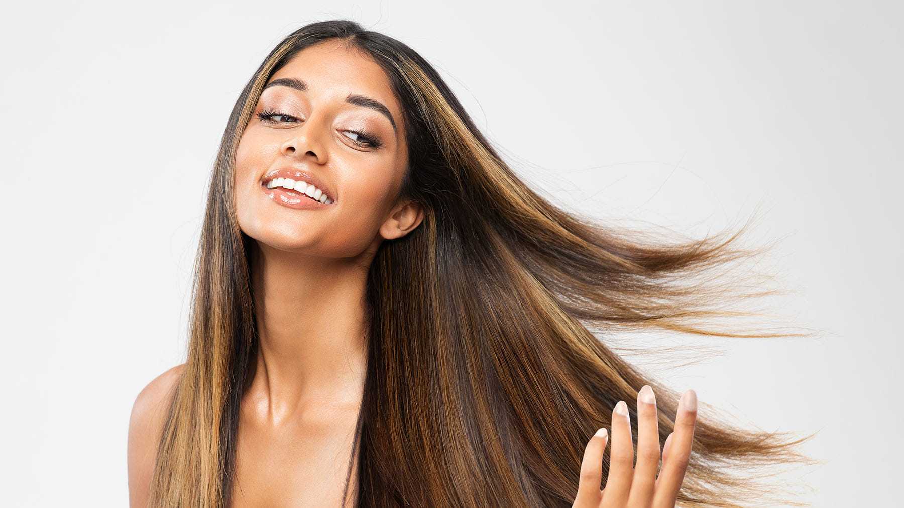 Woman with long, flowing hair smiling and tossing her hair against a white background.