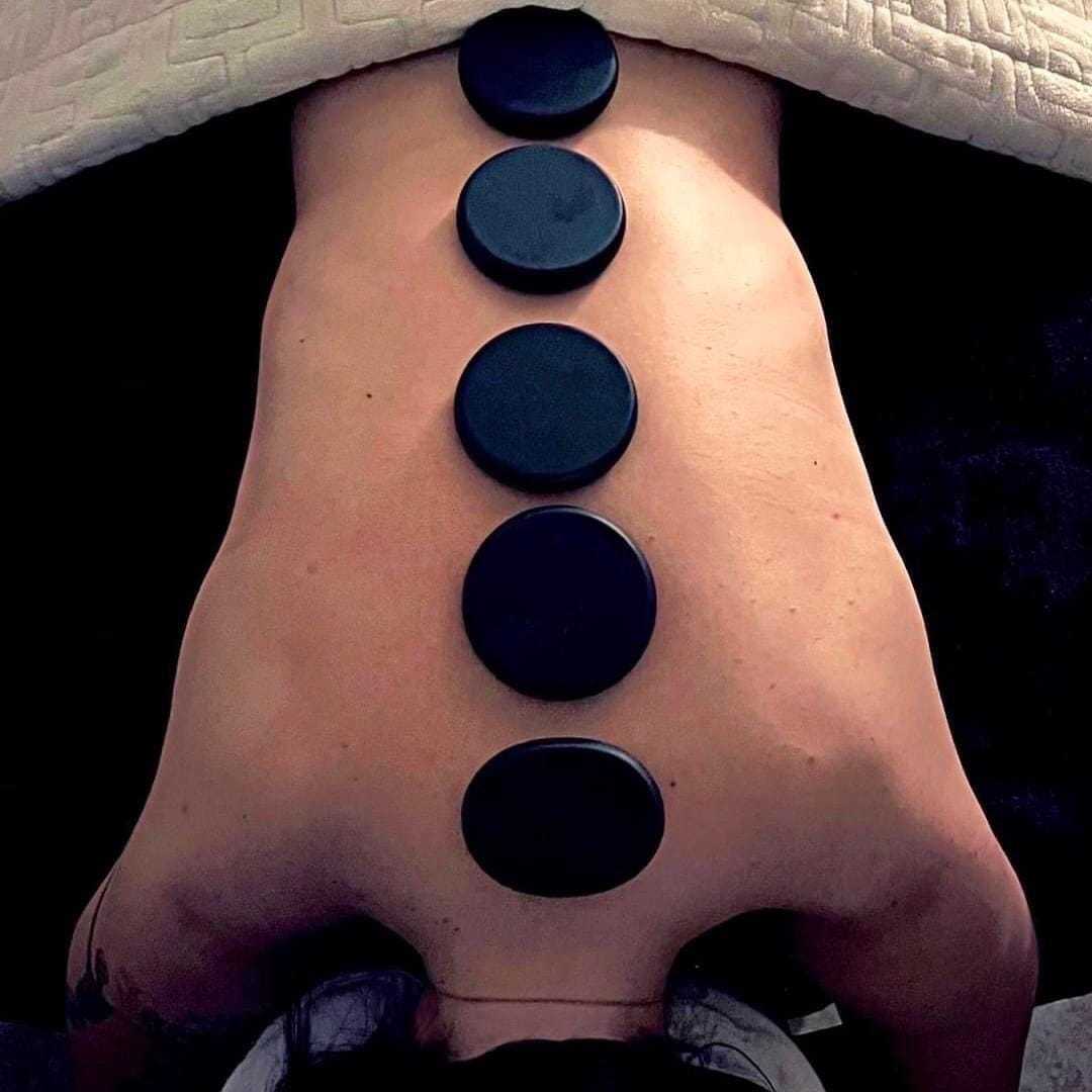 Person receiving a hot stone massage with five stones placed along their back.